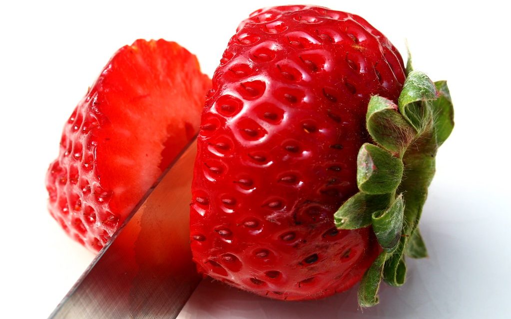 A knife slices through a single red strawberry.
